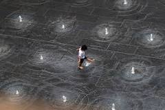 Photograph taken from above of a child playing in a splash pad water fountain.